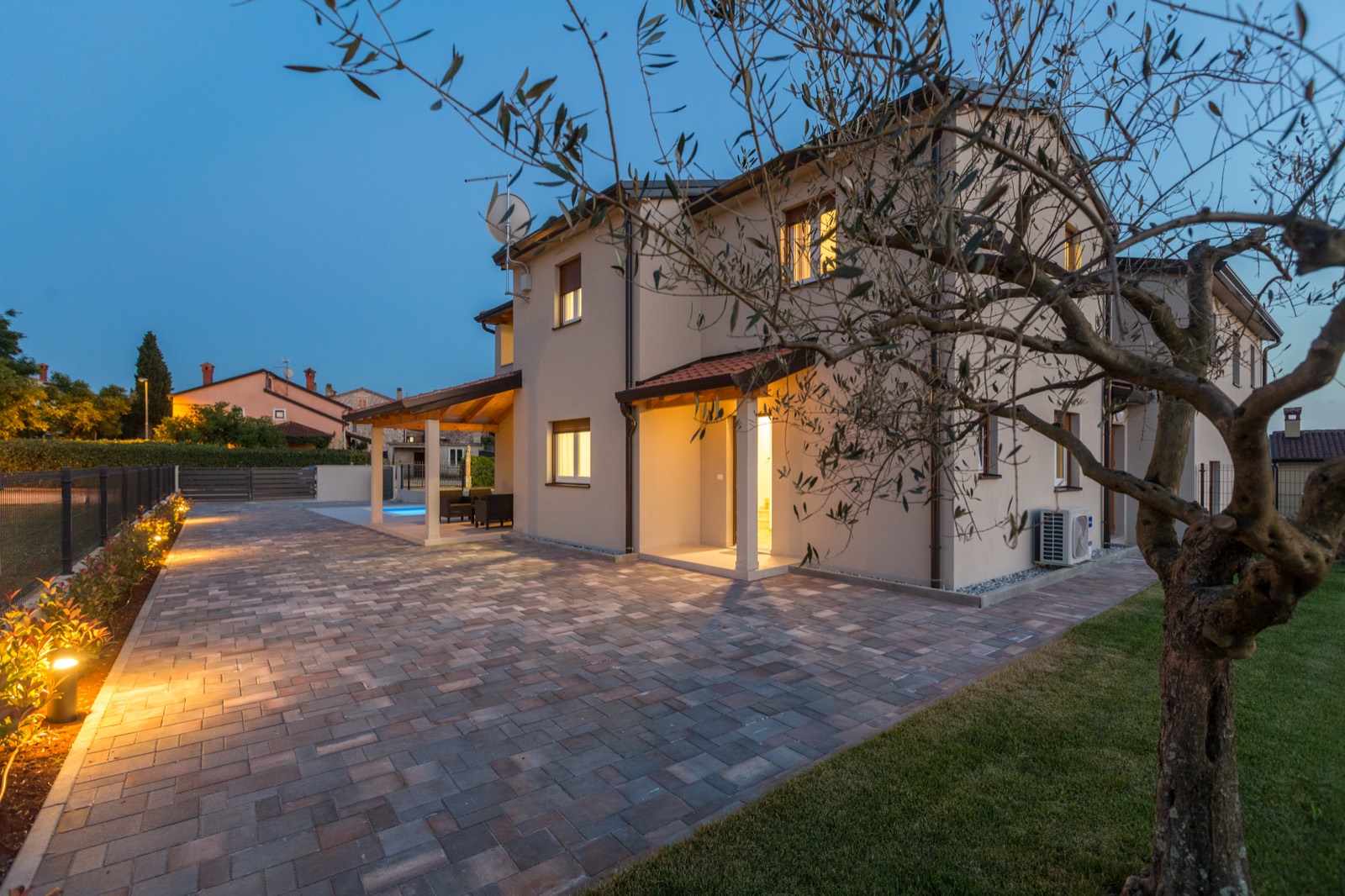 Paved courtyard and olive tree at dusk with the house lit behind